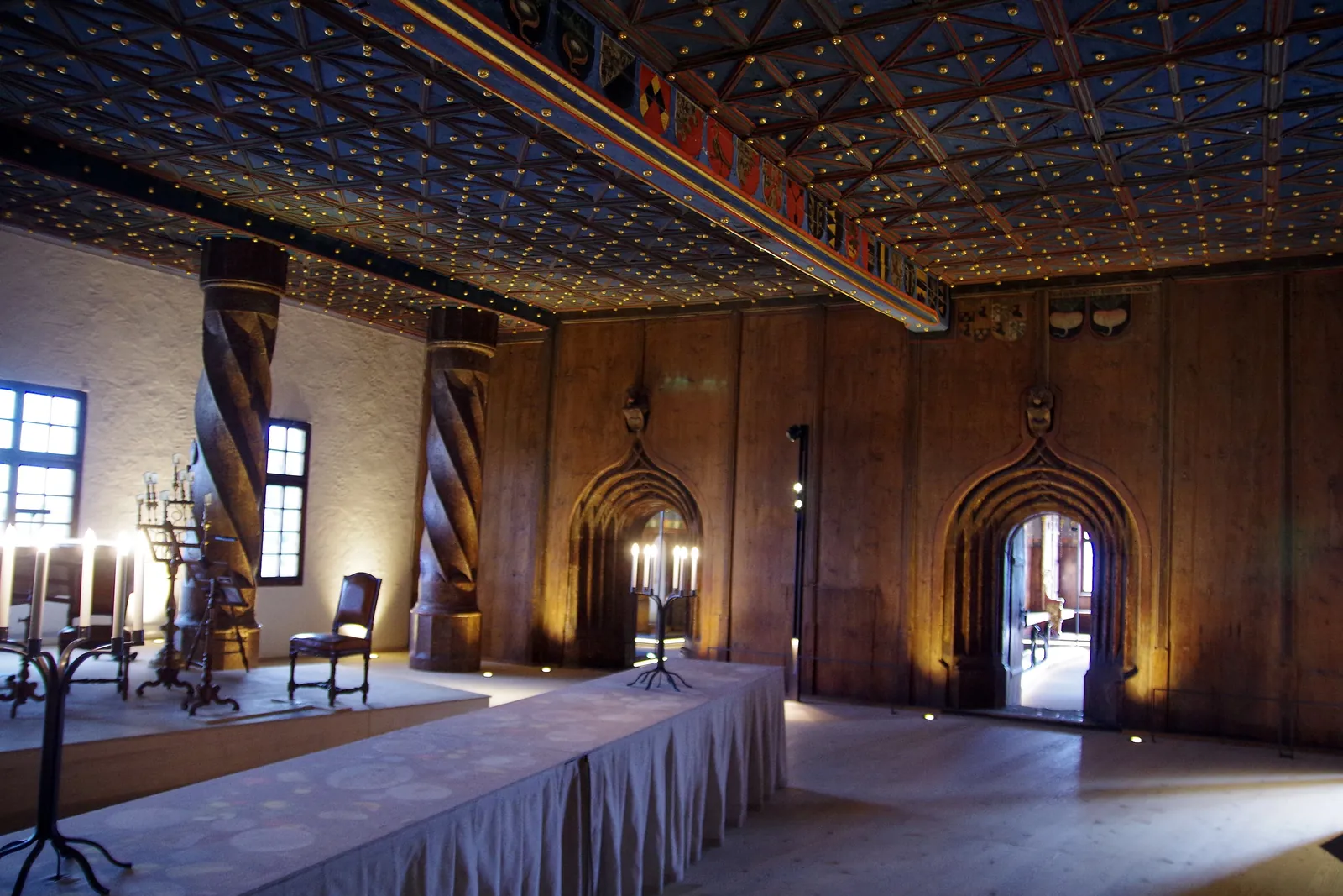 Ein Saal in den Fürstenzimmern der Festung mit einer dunklen Decke, besetzt mit goldenen Sternen, gedrehten Holzsäulen, einem langen Tisch und Kerzenleuchtern
